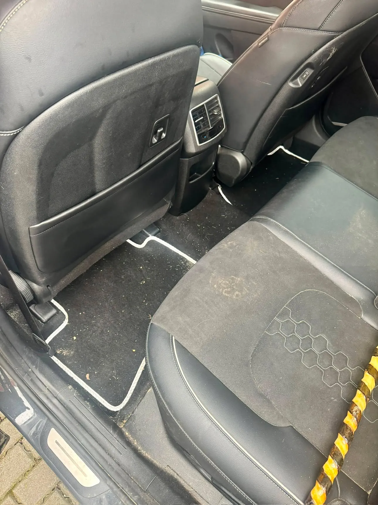 Rear footwell of a grey SUV with grit, leaf litter and dried mud over the mat and carpet.