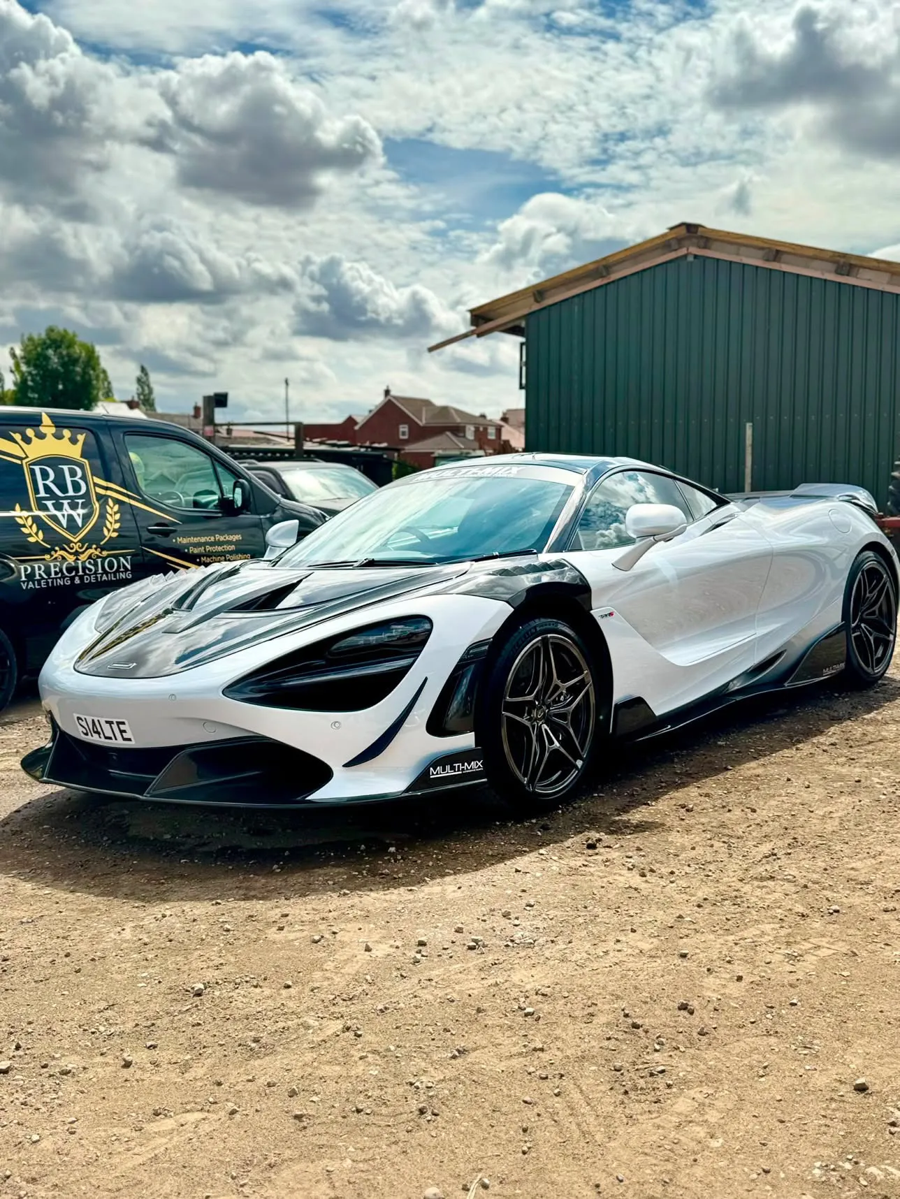 White McLaren 720S freshly detailed, parked in a yard with the black and gold RBW Precision van behind it.