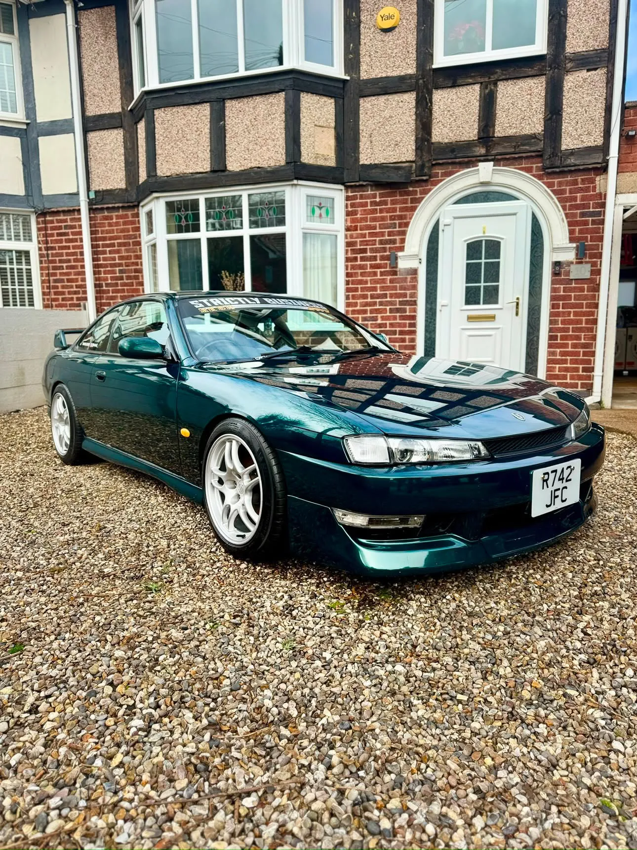 Deep green Nissan 200SX S14a on a gravel driveway, the house behind mirrored in its bonnet after a full detail.