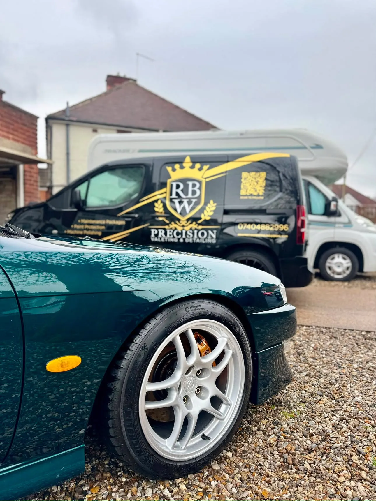 Front wing of a green Nissan S14 in the foreground with the RBW Precision van behind, its gold crest, phone number and QR code on the black bodywork.